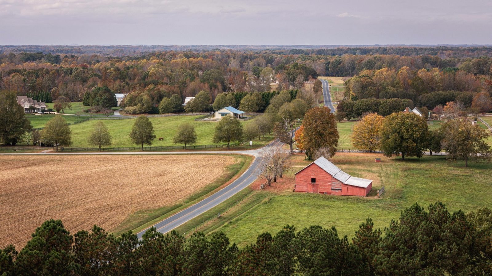 Aerial view of farm fields, a red barn and a winding road in autumn