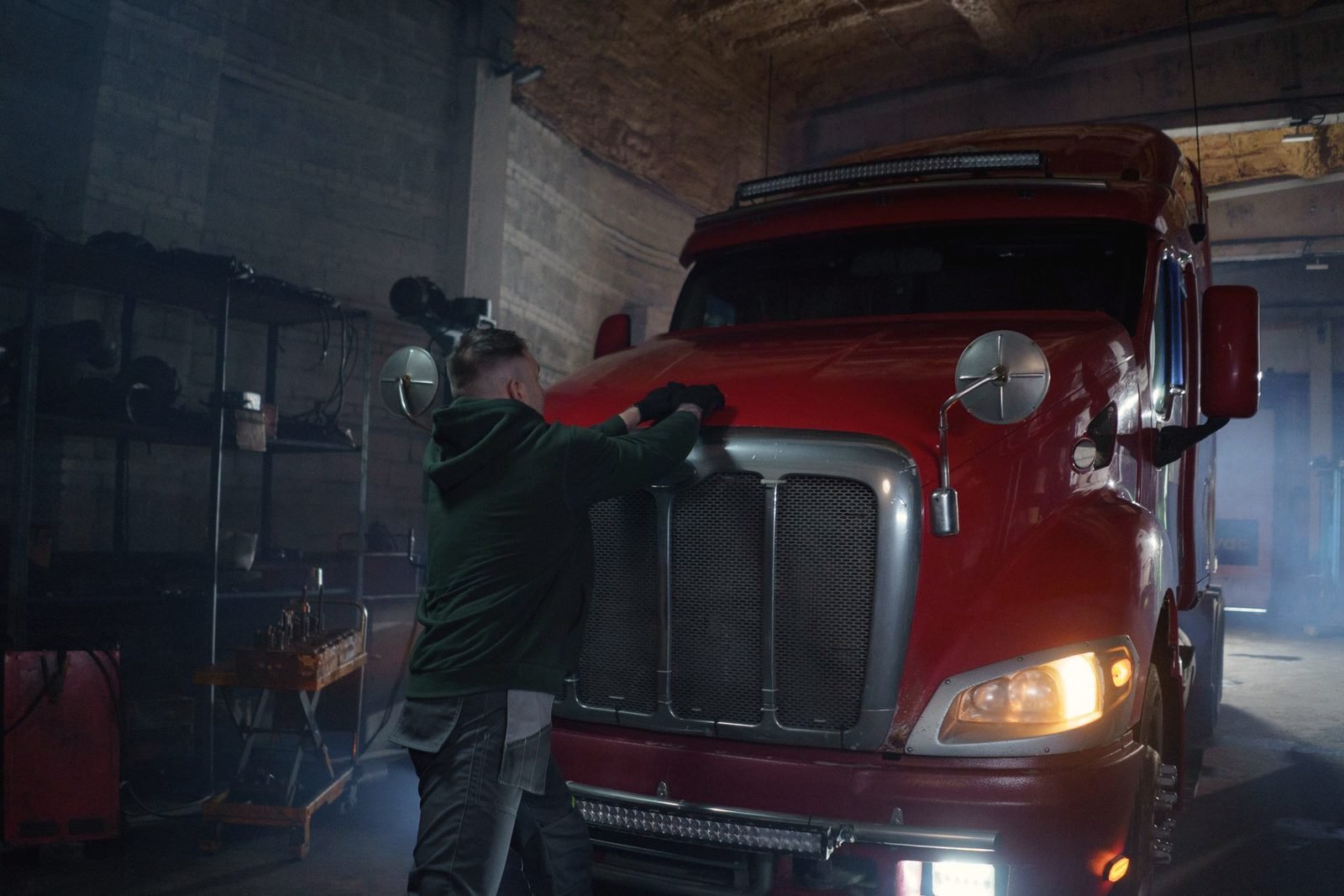 A mechanic, seen from behind, working at the grille of a red tractor