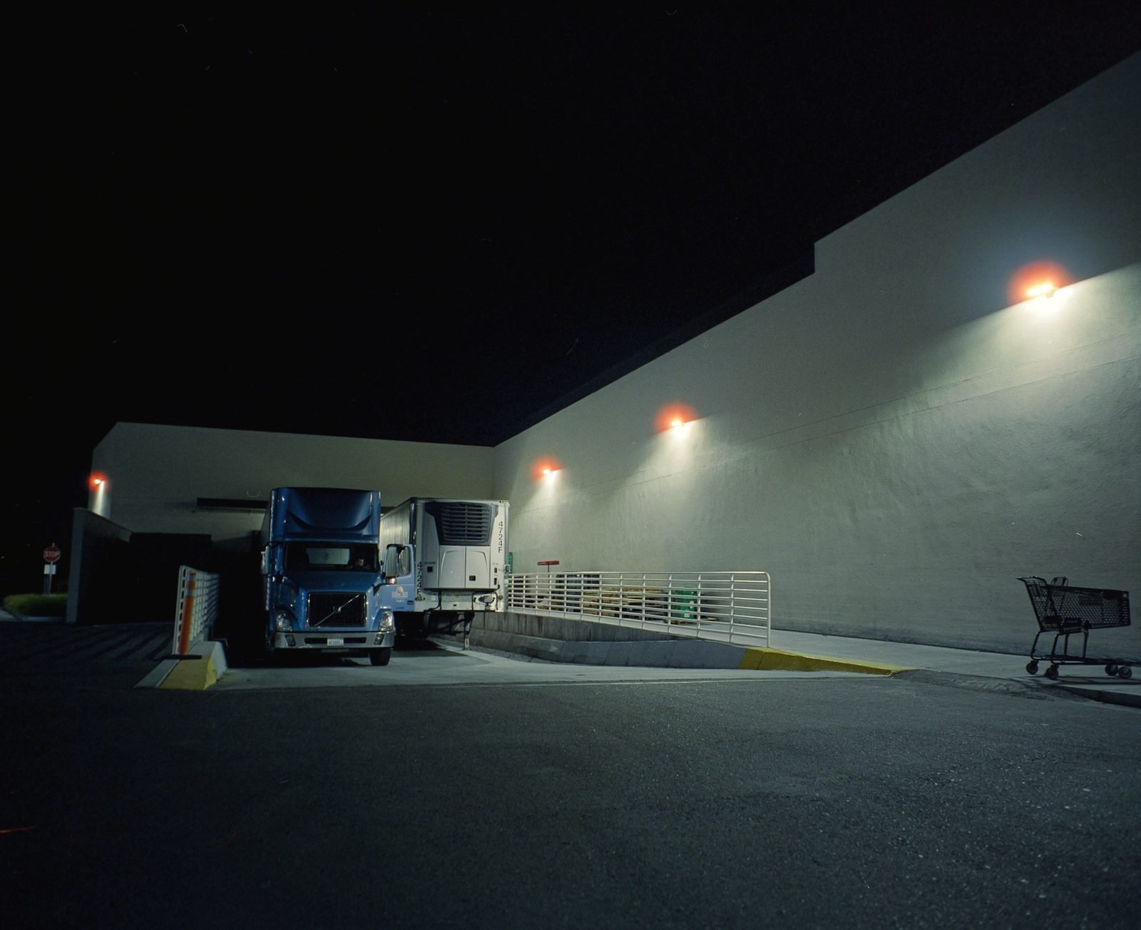 A tractor and reefer trailer at a loading dock under wall lamps at night