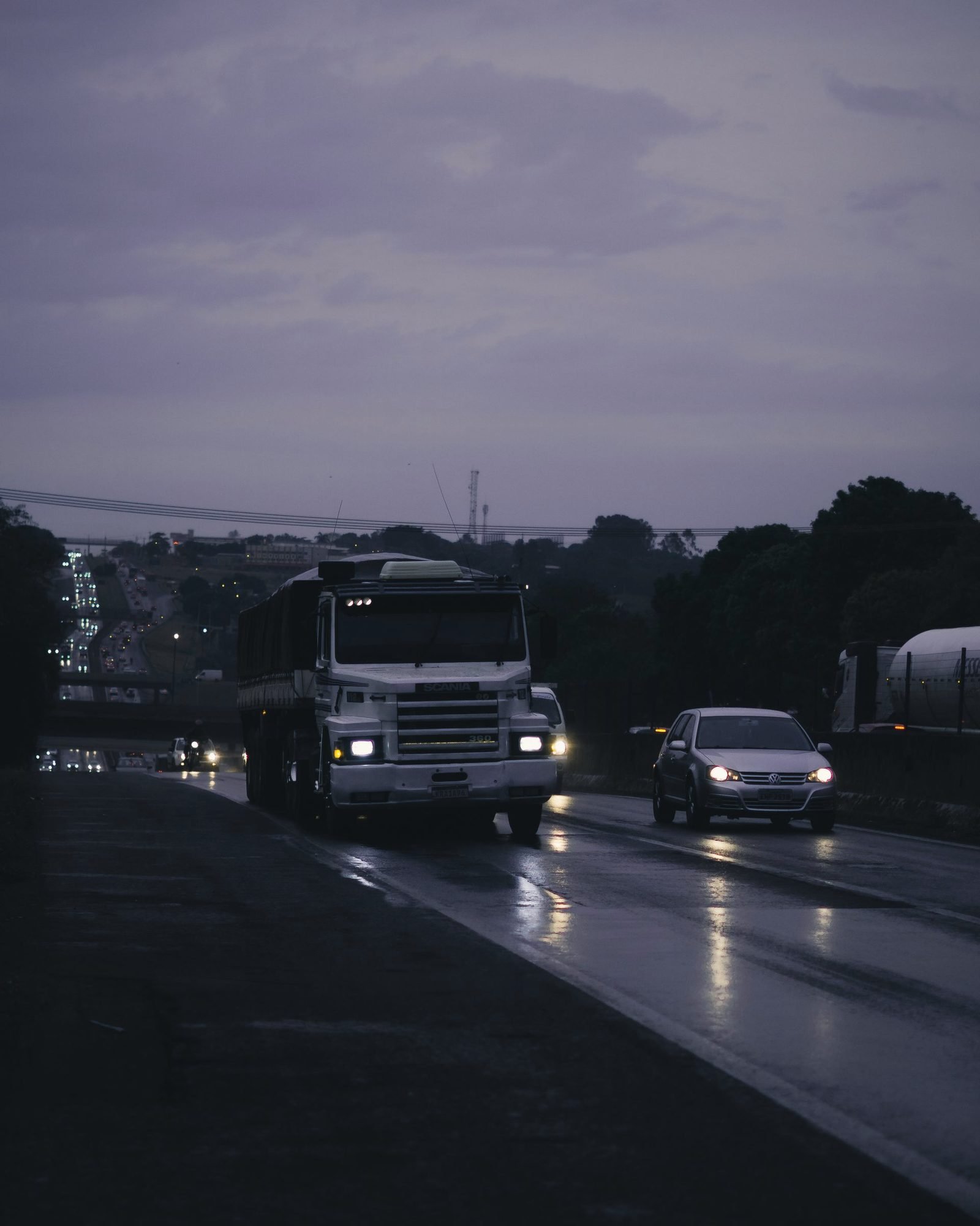A truck with headlights on along a wet highway at dusk
